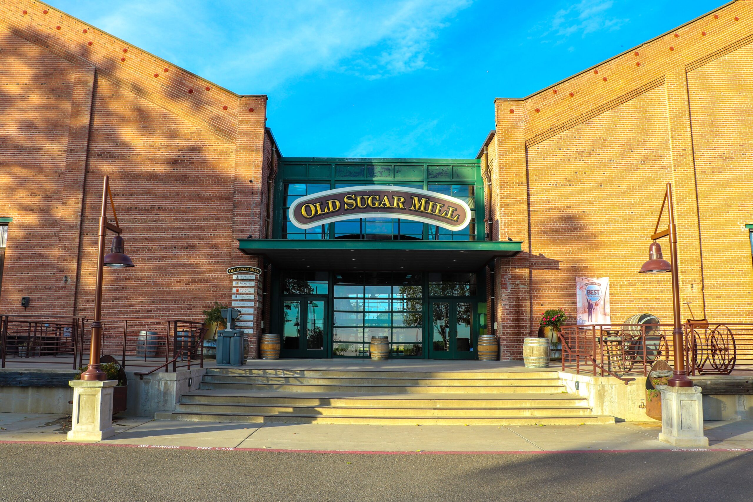 The image depicts a historic brick industrial building with an outdoor courtyard featuring seating areas, where people stroll between doors, enjoying the rustic charm of the space. This setting is ideal for wine lovers seeking intimate tastings and a vibrant atmosphere reminiscent of California's wine country.